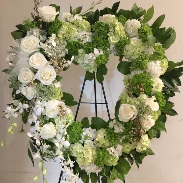 Heart-shaped floral wreath with white roses and green hydrangeas on a stand