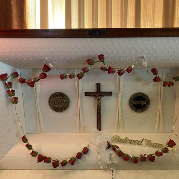 White casket with red rose garland and a crucifix inside