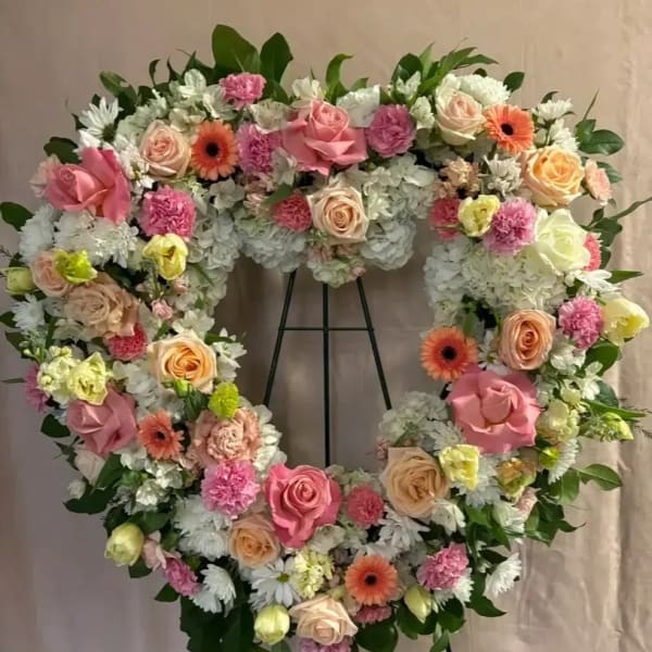 Heart-shaped floral wreath with pink, peach, and white flowers on an easel
