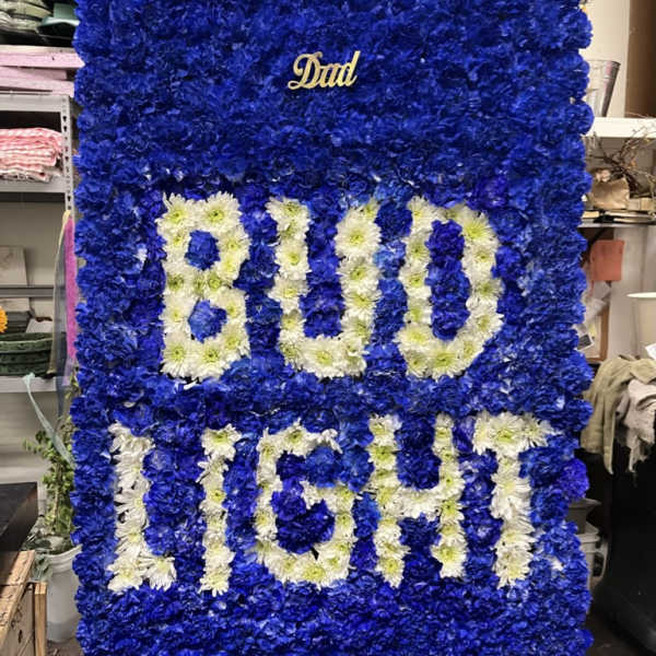 Blue floral tribute board with white flower lettering and a small "Dad" plaque