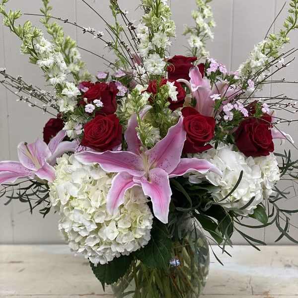 Bouquet of red roses, pink lilies, and white hydrangeas in a glass vase