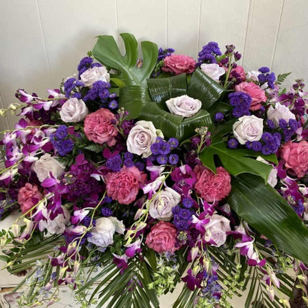 Large floral arrangement with pink roses, purple orchids, and broad tropical leaves