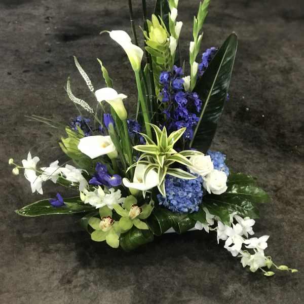 Tall floral arrangement with white calla lilies, blue hydrangea, and white orchids