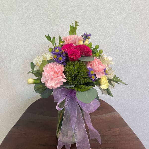 Mixed pink and purple bouquet in a glass vase with a lavender ribbon