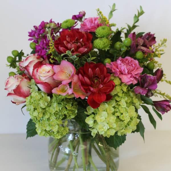 Mixed arrangement of red and pink blooms with green hydrangeas in a clear glass vase