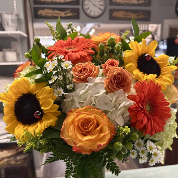 Bouquet of sunflowers, orange roses, and white hydrangeas in a glass vase