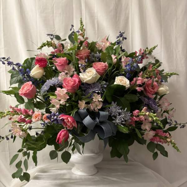 Large mixed flower arrangement in a white pedestal vase with a blue ribbon