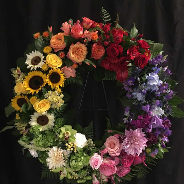 Colorful floral wreath with roses, sunflowers, and purple blooms on a black stand