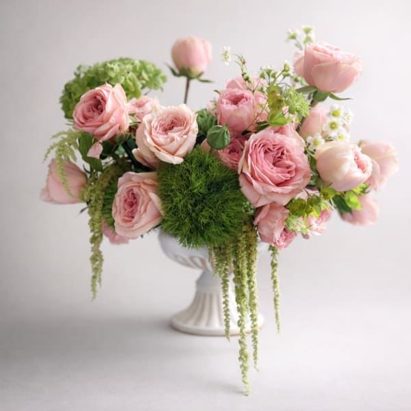 Low arrangement of pink roses and mixed blooms in a white pedestal vase