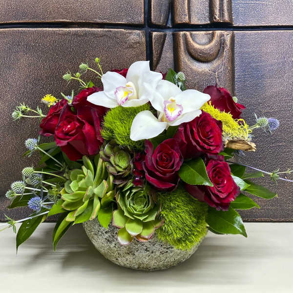 Red roses and white orchids in a stone bowl with succulents