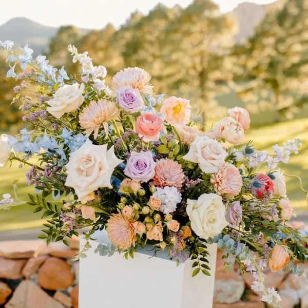 Pastel floral arrangement with roses and daisies in a white pedestal vase