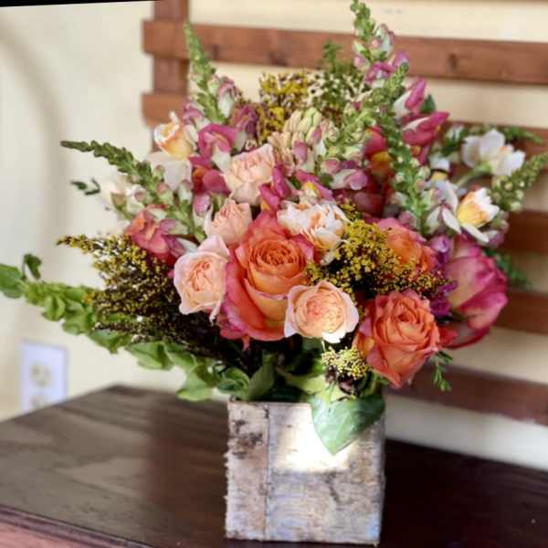 Bouquet of peach and pink roses with tall pink snapdragons in a birch vase