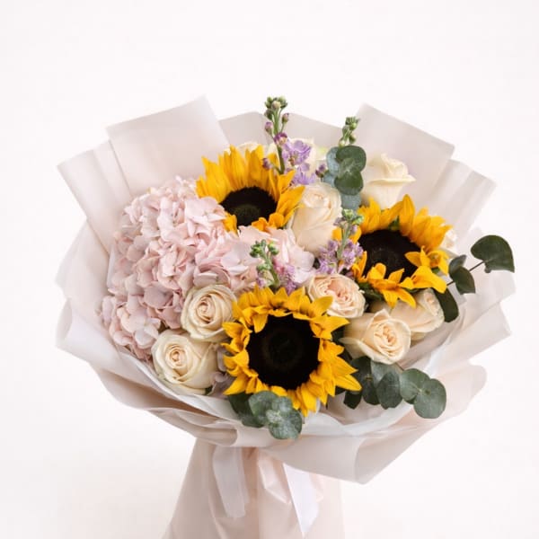 Bouquet of sunflowers, pale roses, and pink hydrangea wrapped in white paper