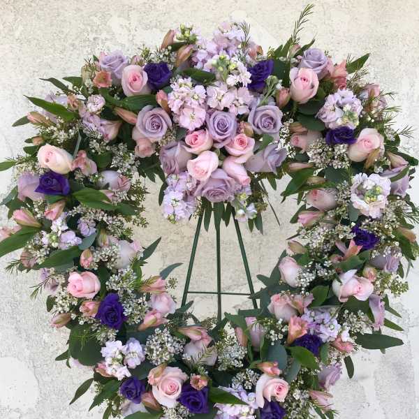 Heart-shaped floral wreath with pink and lavender roses on a stand