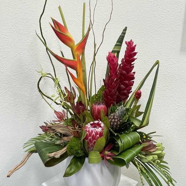 Tropical floral arrangement with red and orange blooms in a white vase