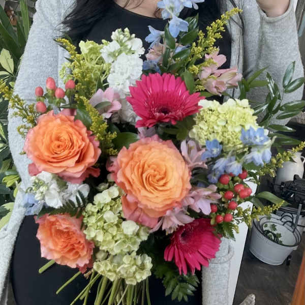 Handheld bouquet with orange roses, pink gerberas, and blue flowers