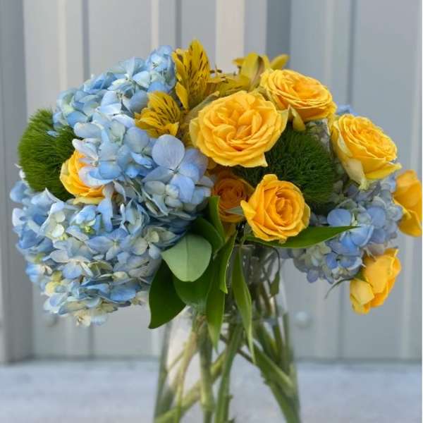Bouquet of blue hydrangeas and yellow roses in a clear glass vase