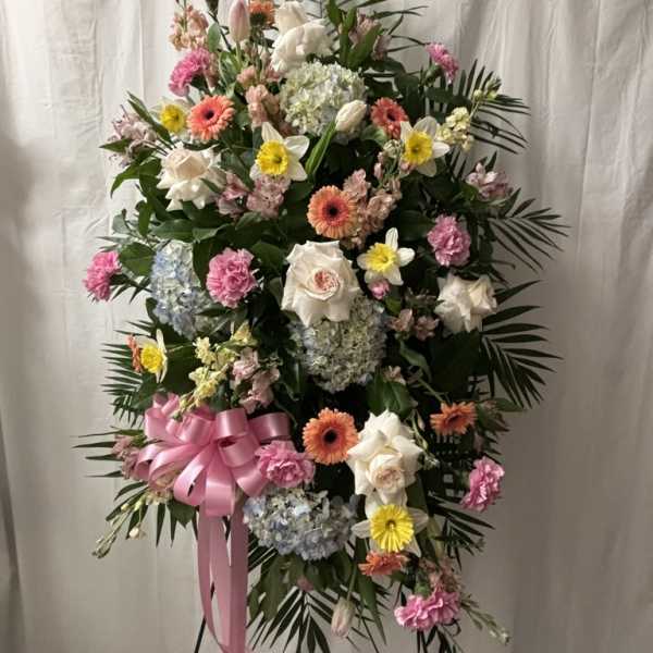 Standing floral spray with pink, white, and yellow blooms and a pink ribbon
