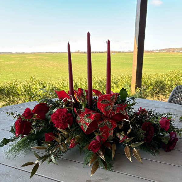 Red floral centerpiece with three tall candles on a table