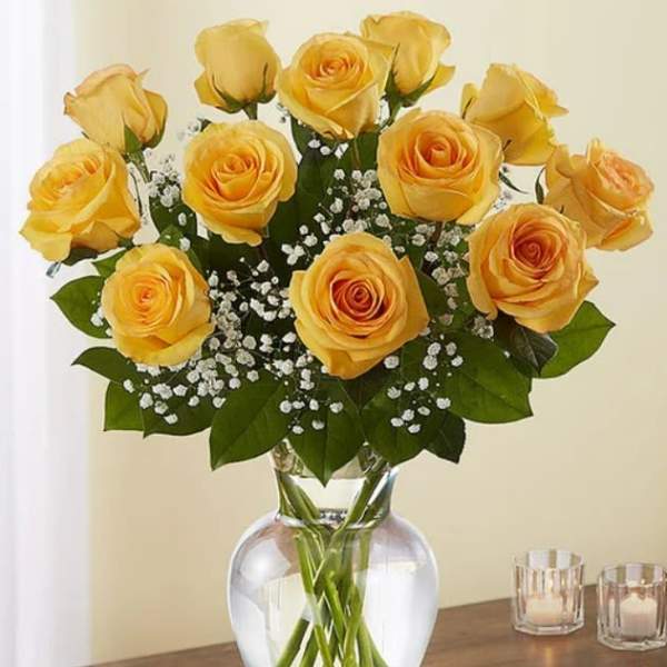 Dozen yellow roses with white filler flowers arranged in a clear glass vase