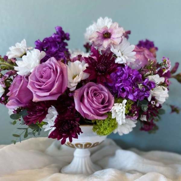 Purple and white floral arrangement in a white pedestal vase