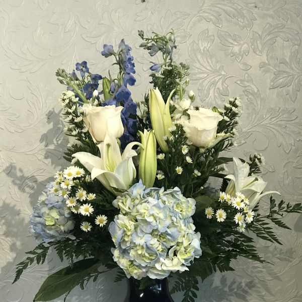 White lilies, roses, and blue flowers in a dark vase