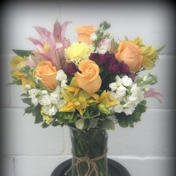 Mixed bouquet of peach roses, pink lilies, and white blooms in a glass vase