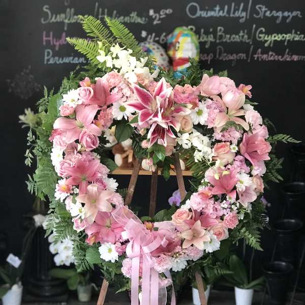 Heart-shaped pink floral wreath on an easel with a ribbon bow