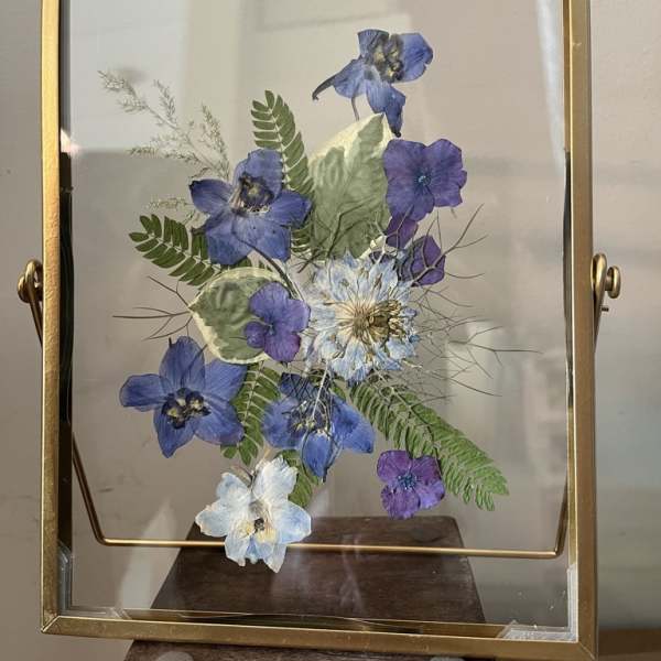 Framed pressed blue and purple flowers with fern leaves in a gold frame