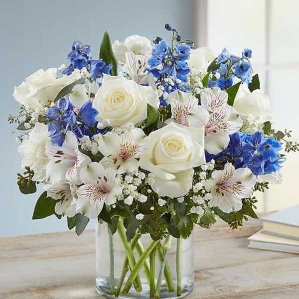 White roses and blue flowers arranged in a clear glass vase
