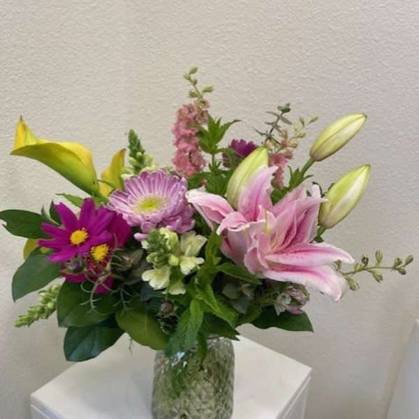 Mixed bouquet of pink lilies and purple flowers in a glass vase
