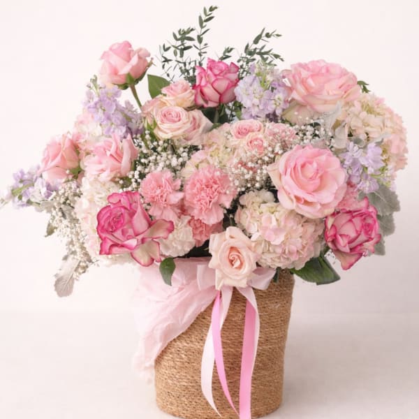 Pink and cream rose bouquet in a woven basket with ribbon