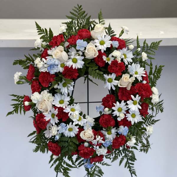 Circular funeral wreath with red, white, and blue flowers on a stand