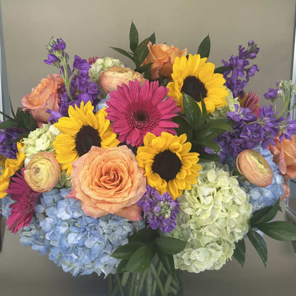 Colorful bouquet with sunflowers, roses, gerbera daisies, and hydrangeas in a glass vase