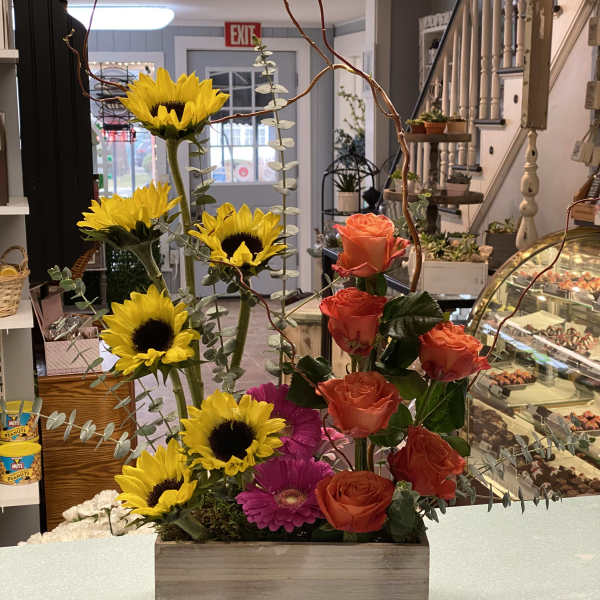 Mixed bouquet with sunflowers, orange roses, and pink gerbera daisies in a wooden box