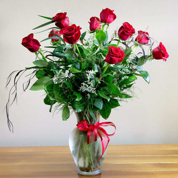 Arrangement of long-stemmed red roses with white filler flowers in a clear glass vase tied with a red ribbon