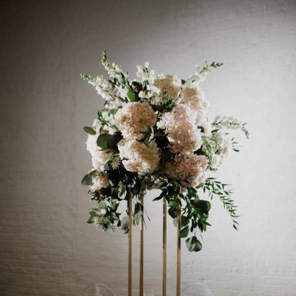 Tall floral centerpiece with blush and white blooms on a gold stand