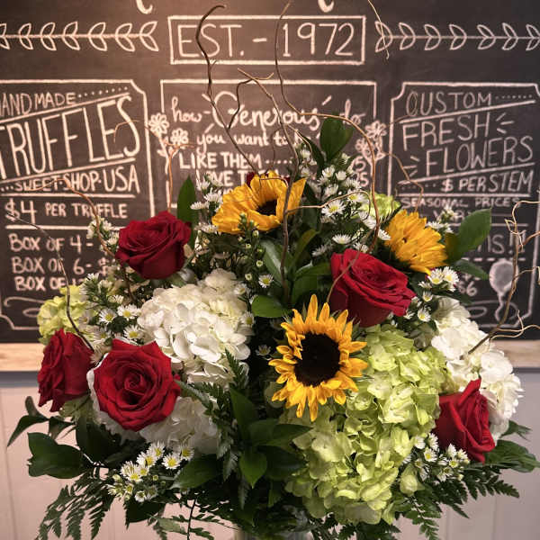 Bouquet of red roses, sunflowers, and hydrangeas in a glass vase