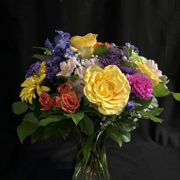 Mixed bouquet of roses, daisies, and purple flowers in a glass vase