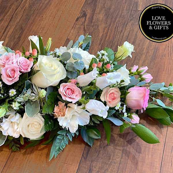 Long, low centerpiece of pink and white roses with lisianthus and small white daisies.