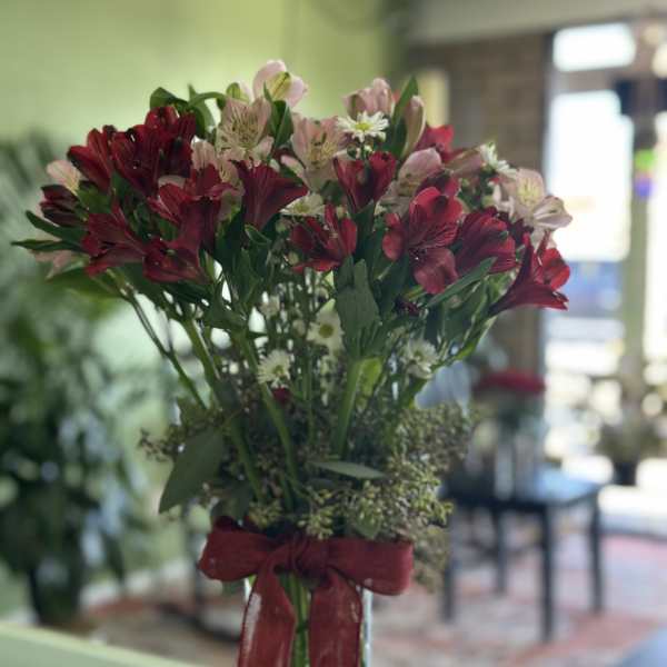 Bouquet of red and pink alstroemeria in a clear glass vase with a red ribbon