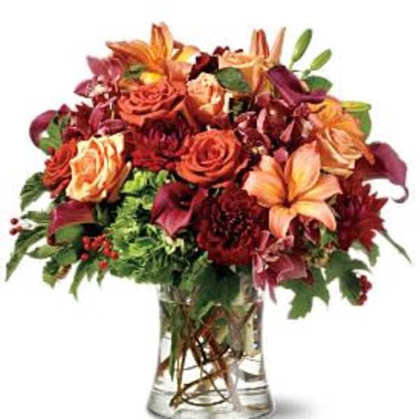 Mixed bouquet of orange, red, and peach flowers in a clear glass vase