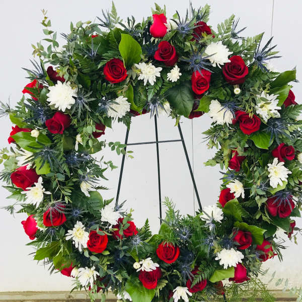 Large heart-shaped floral wreath with red roses and white daisies on a stand