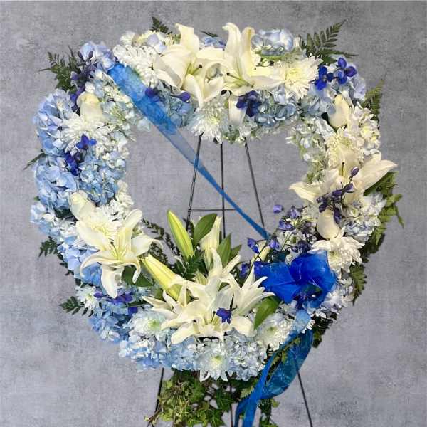 Heart-shaped floral wreath with white lilies and blue flowers on a stand