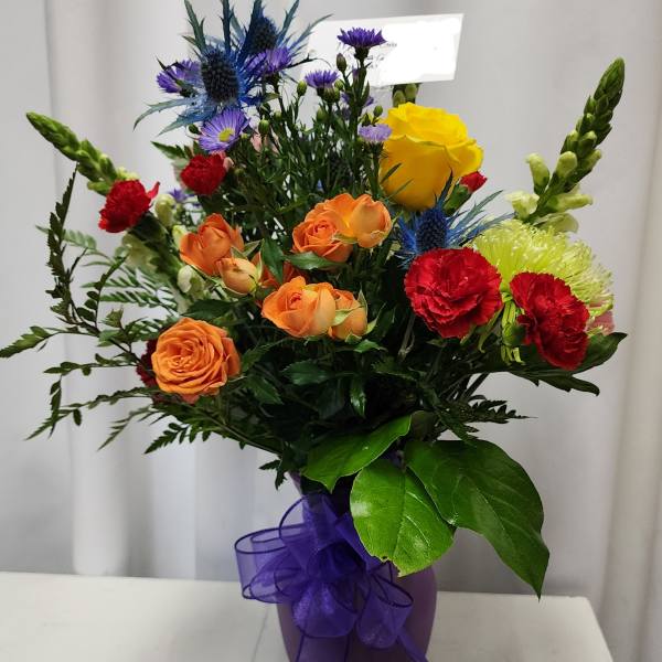 Mixed bouquet of roses, carnations, and blue thistle in a purple vase