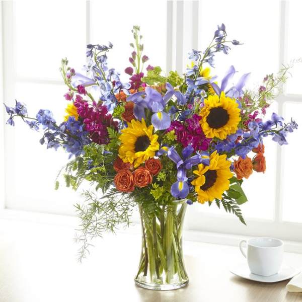 Bouquet of sunflowers, blue irises, and orange roses in a clear glass vase