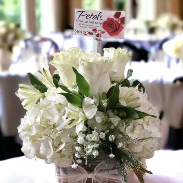 White floral arrangement in a square glass vase with a ribbon