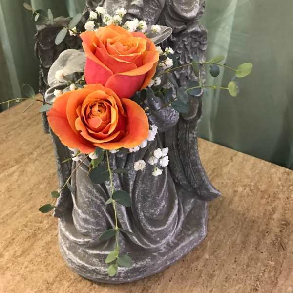 Two orange roses arranged on a stone angel statue