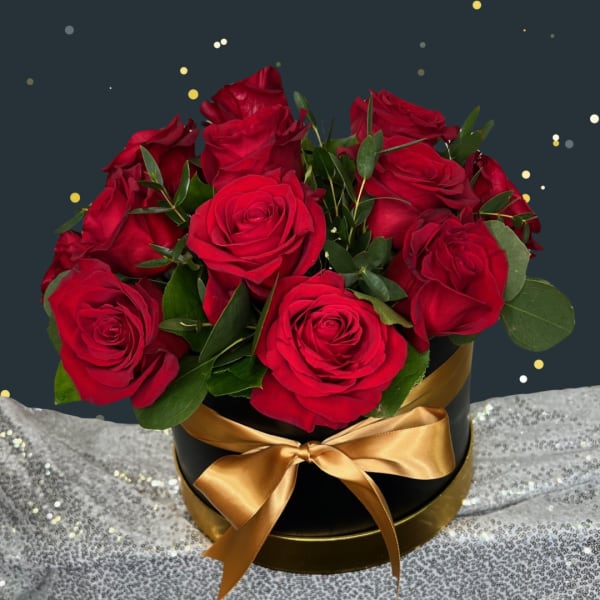 Red roses arranged in a black round box with a gold ribbon