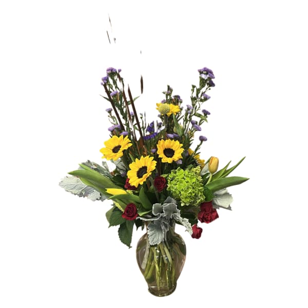 Mixed bouquet with sunflowers, red roses, and purple filler in a glass vase